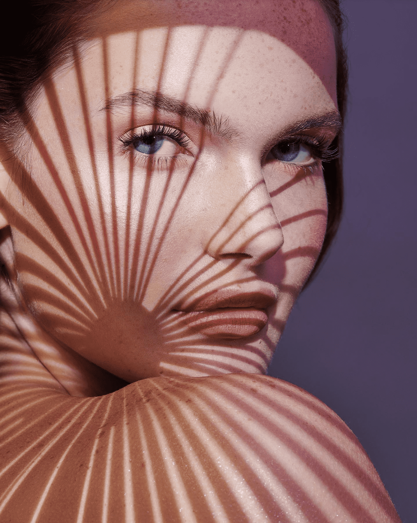 Shadow lines on a models face with purple mauve background and medium deep blue eyes.
